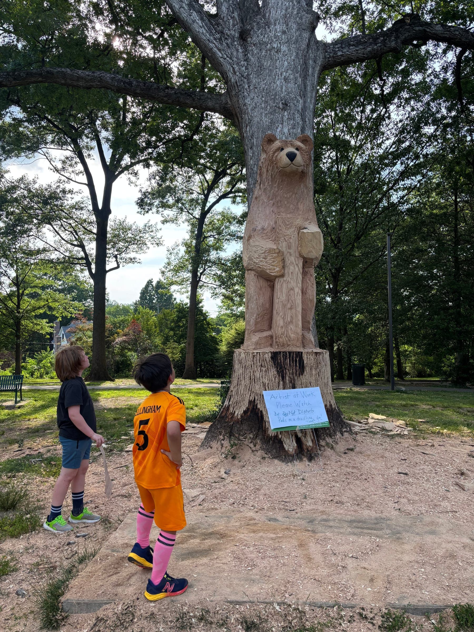 Two children looking up at the nearly finished bear carving
